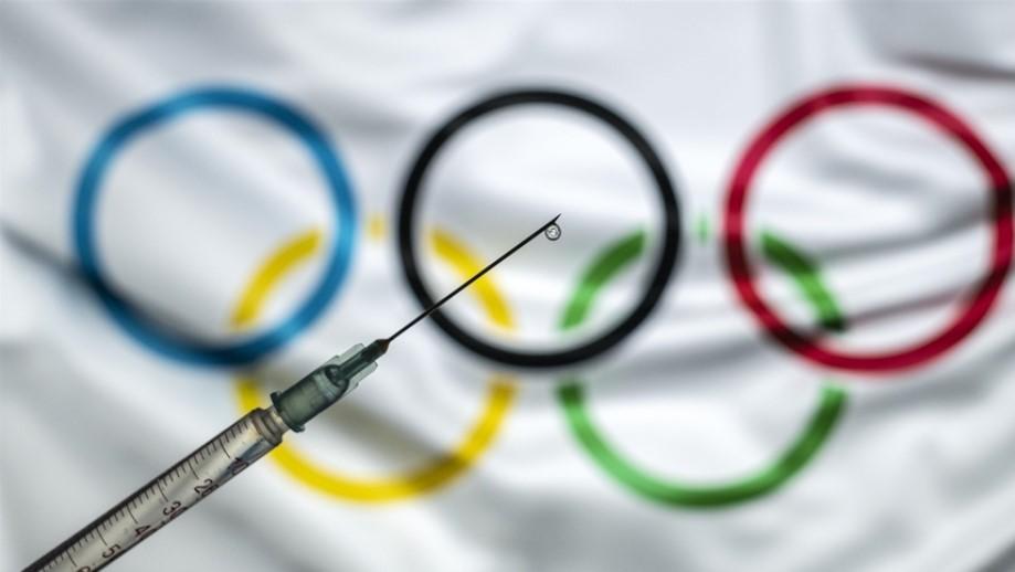 In this photo illustration taken in Ankara, Turkey on December 30, 2020 a vaccine syringe with a drop on the needle's end is seen in front of a computer screen showing the flag of International Olympic Committee (IOC) - Avaz